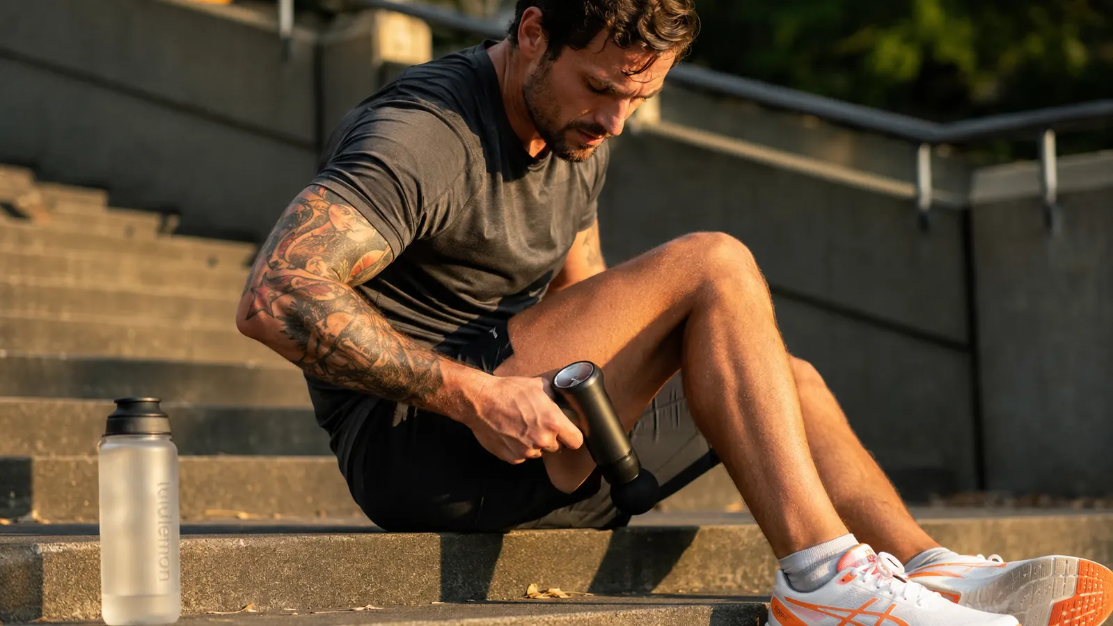Person using a massage gun on their calf muscles after a run, sitting on outdoor steps
