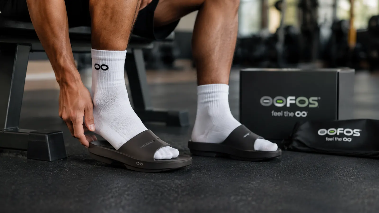 Person slipping on OOFOS OOahh recovery slides immediately after removing running shoes post-workout