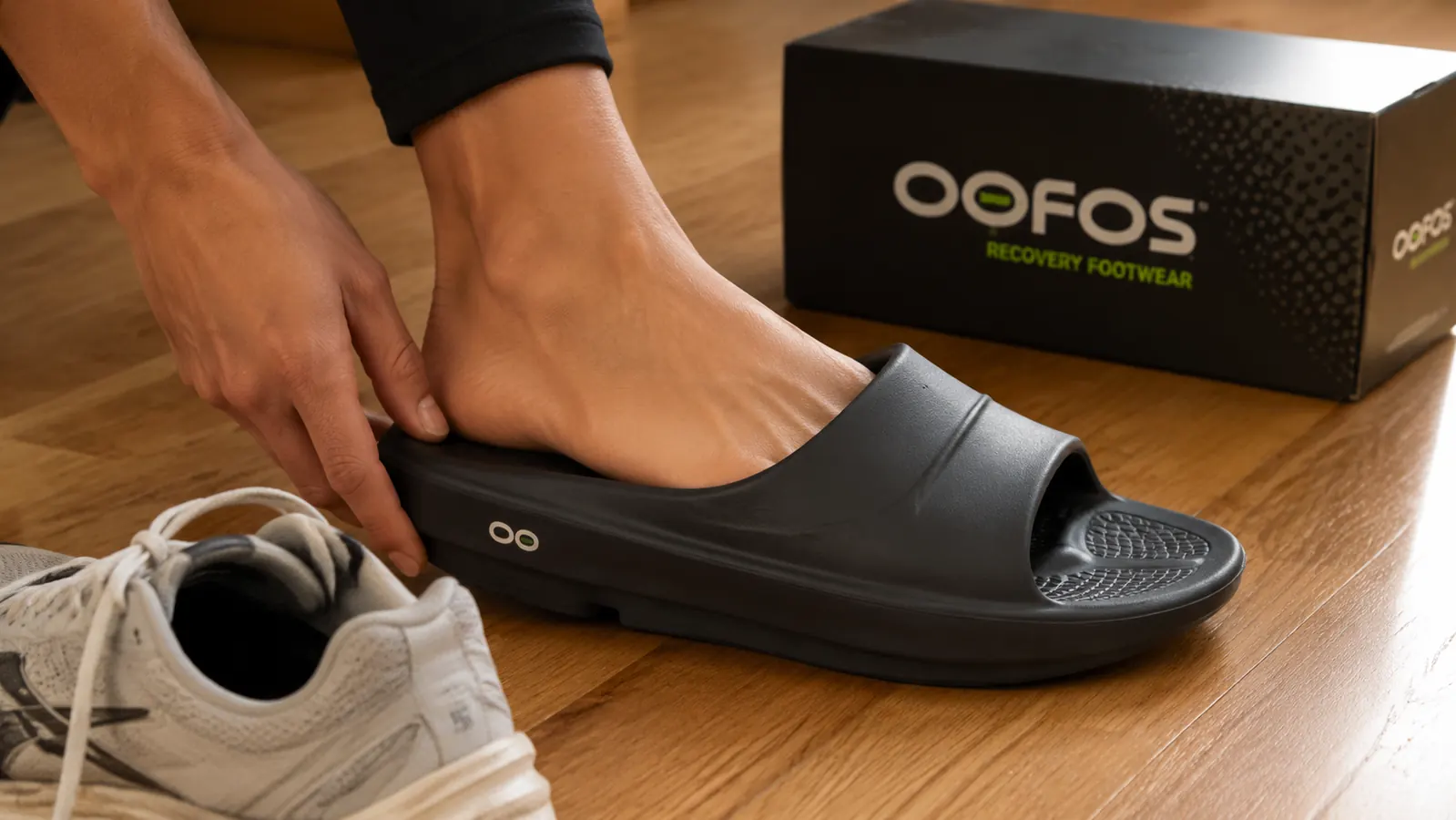 Close-up of a foot sliding into an OOFOS OOahh recovery slide immediately after a run, showing the deep arch contour and foam footbed
