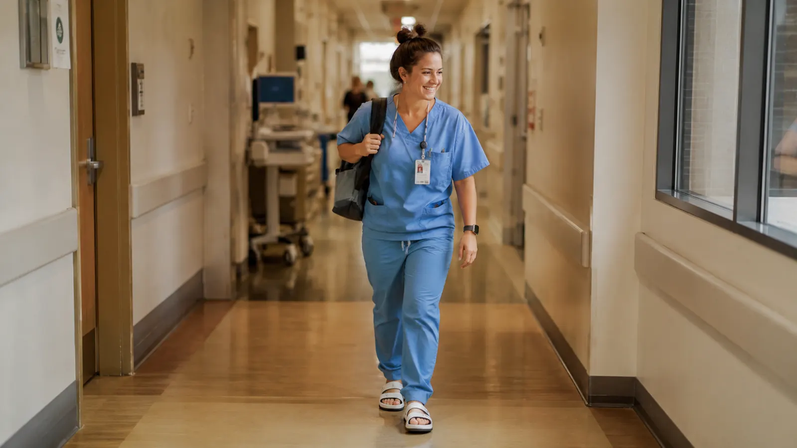 Nurse in scrubs walking through a hospital corridor wearing recovery slides after a shift