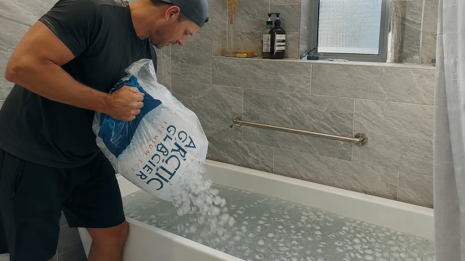 Person reluctantly pouring a bag of ice into a bathtub to prepare a cold plunge